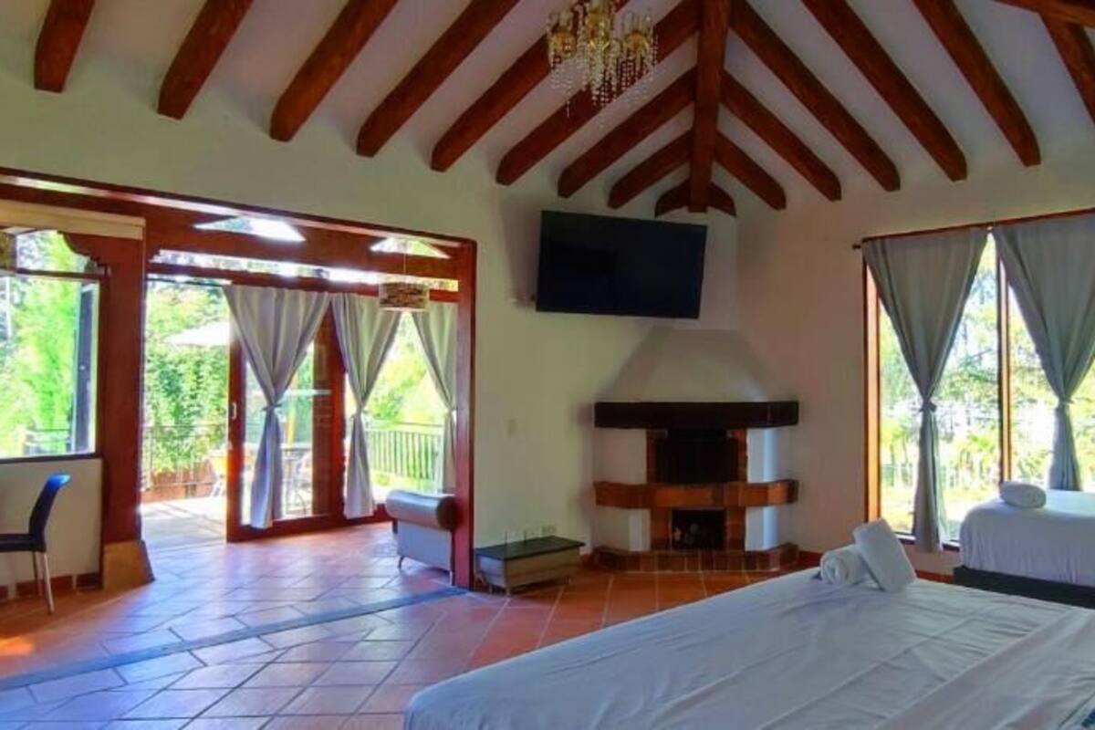Un dormitorio con cama, televisor, chimenea y balcón con cortinas.