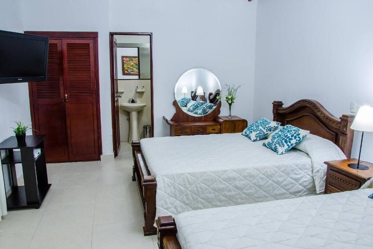 Un dormitorio con dos camas, televisión, armario, espejo y mesita de noche con lámpara.