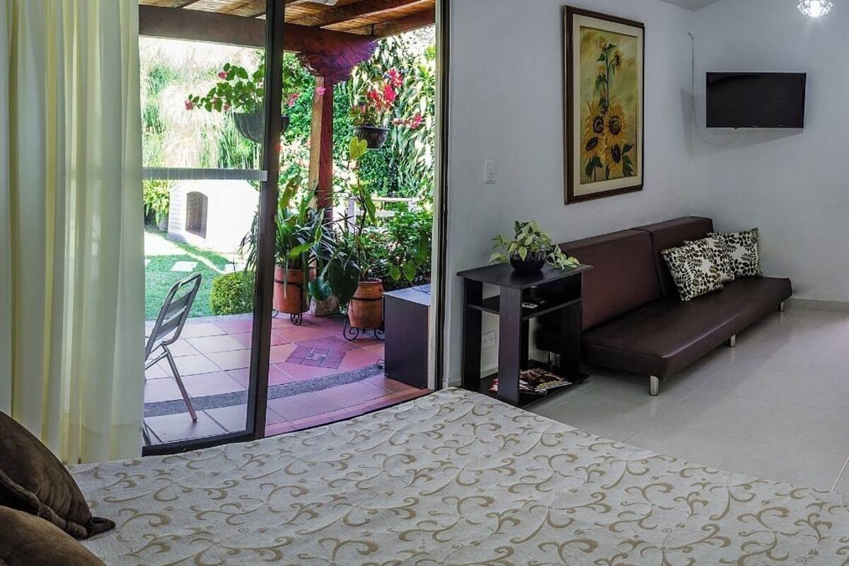 Un dormitorio con cama, sofá, televisor y vistas a un jardín a través de una puerta corredera.