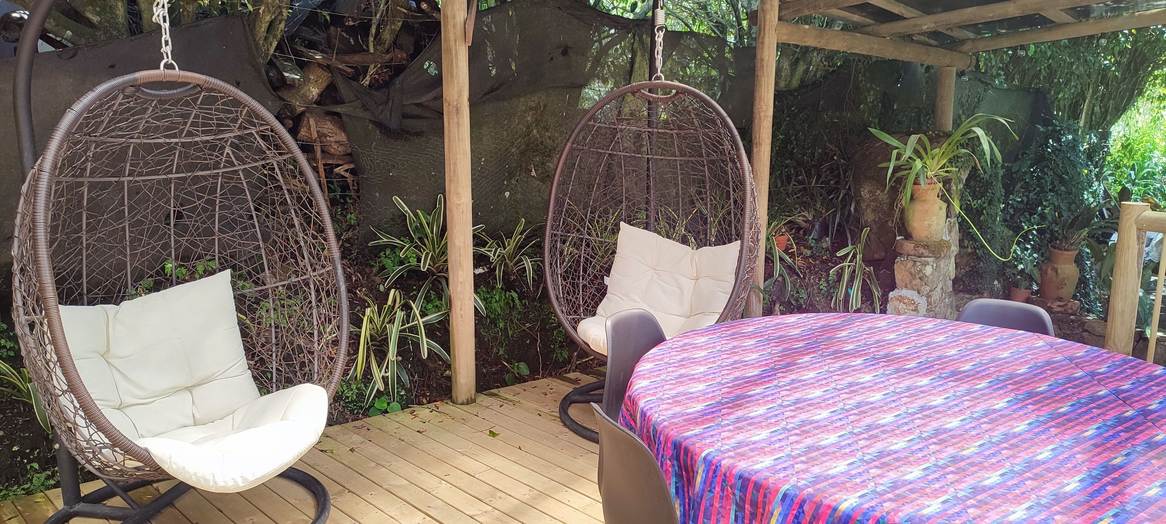 A wooden deck with two hanging chairs and a table with a colorful tablecloth.