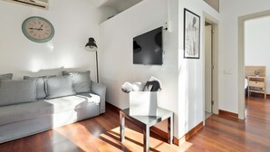 Ein modernes Wohnzimmer mit einem grauen Sofa, einem weißen Couchtisch, einem Flachbildfernseher und einem gerahmten Kunstwerk an der Wand.