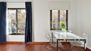 Ein modernes Zimmer mit einem Glastisch, klaren Stühlen und Blick auf eine Stadtlandschaft durch große Fenster.