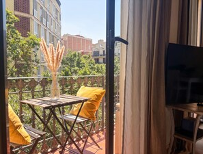 A balcony with a table, chairs, a vase with pampas grass, and a yellow cushion.