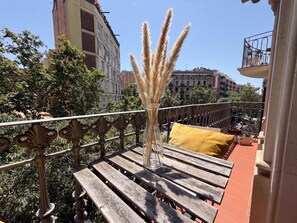 Ein Balkon mit einer Holzbank, einer Vase mit Pampasgras und einem gelben Kissen.