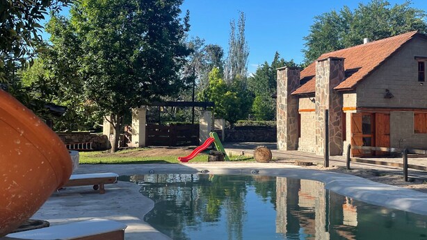 A swimming pool with a slide, surrounded by stone buildings and trees. - Paihuen Luxury Suites (Los Reartes)