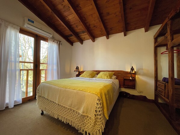 A bedroom with a bed, wooden ceiling beams, a window with curtains, and a bedside table with a lamp. - Paihuen Luxury Suites (Los Reartes)