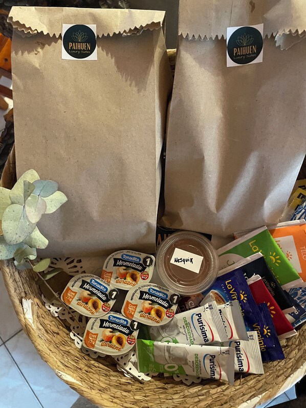 A gift basket with paper bags labeled "Paihuen Luxury Suites," containing various food items and a bottle of NeSquiK.