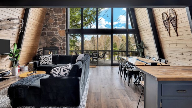 Un'elegante camera in stile loft con parete in pietra, divano in pelle nera, tavolo da pranzo in legno e ampie finestre che si affacciano su alberi.