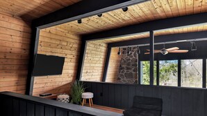 Un interno moderno caratterizzato da pareti in legno, un'ampia finestra, un divano nero e una TV a parete.
