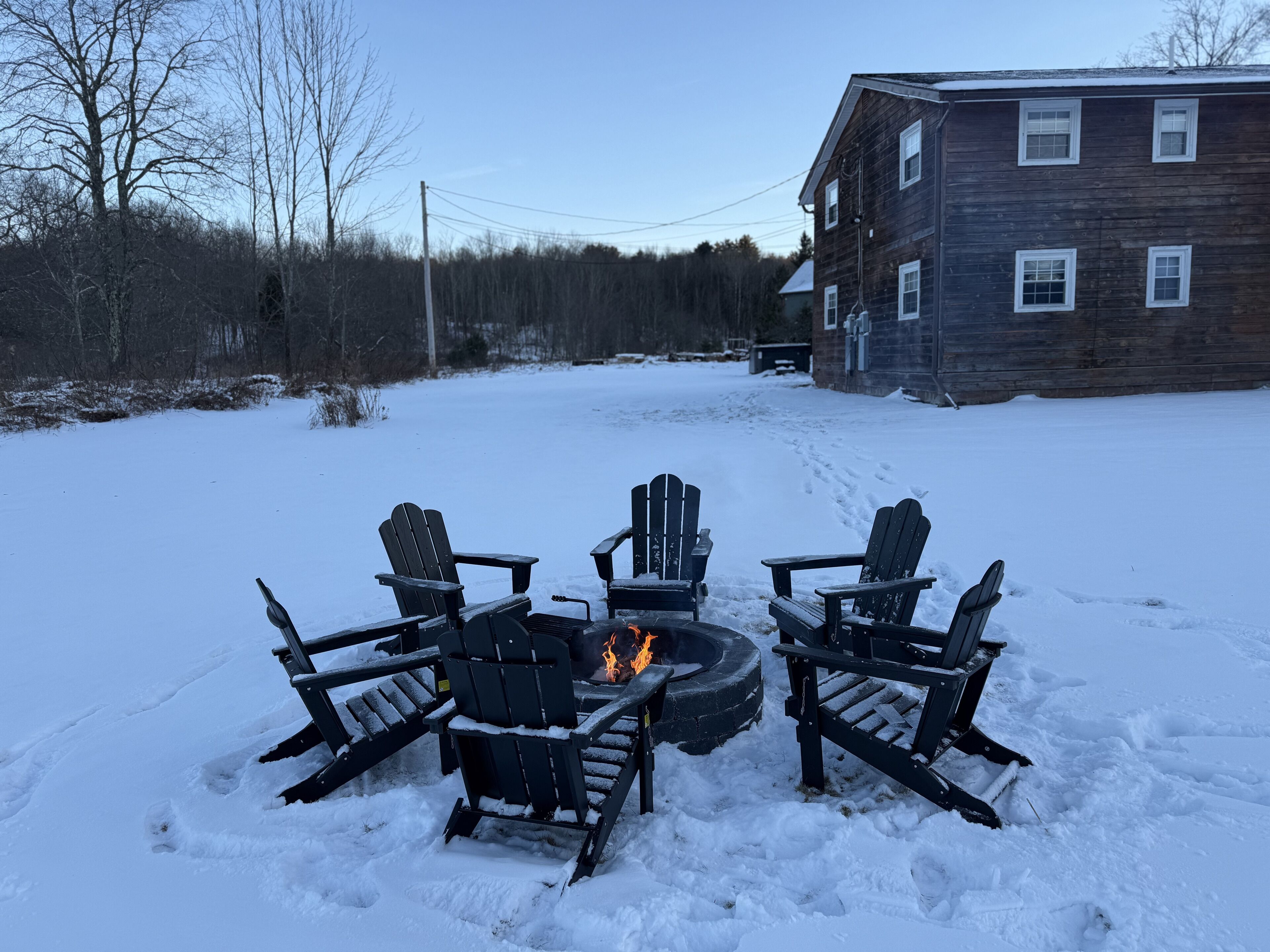Zona exterior nevada con un hoyo de fuego y cuatro sillas Adirondack dispuestas alrededor.