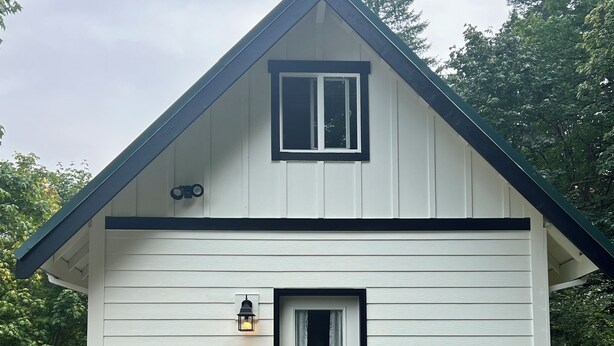 A white house with a dark roof, a front door, and two potted plants on either side. - The Little Tiny Cabin "LTC" (Deming)