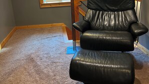 A black leather chair in a room with a sloped ceiling, a window, and a floor lamp. - The Little Tiny Cabin "LTC" (Deming)
