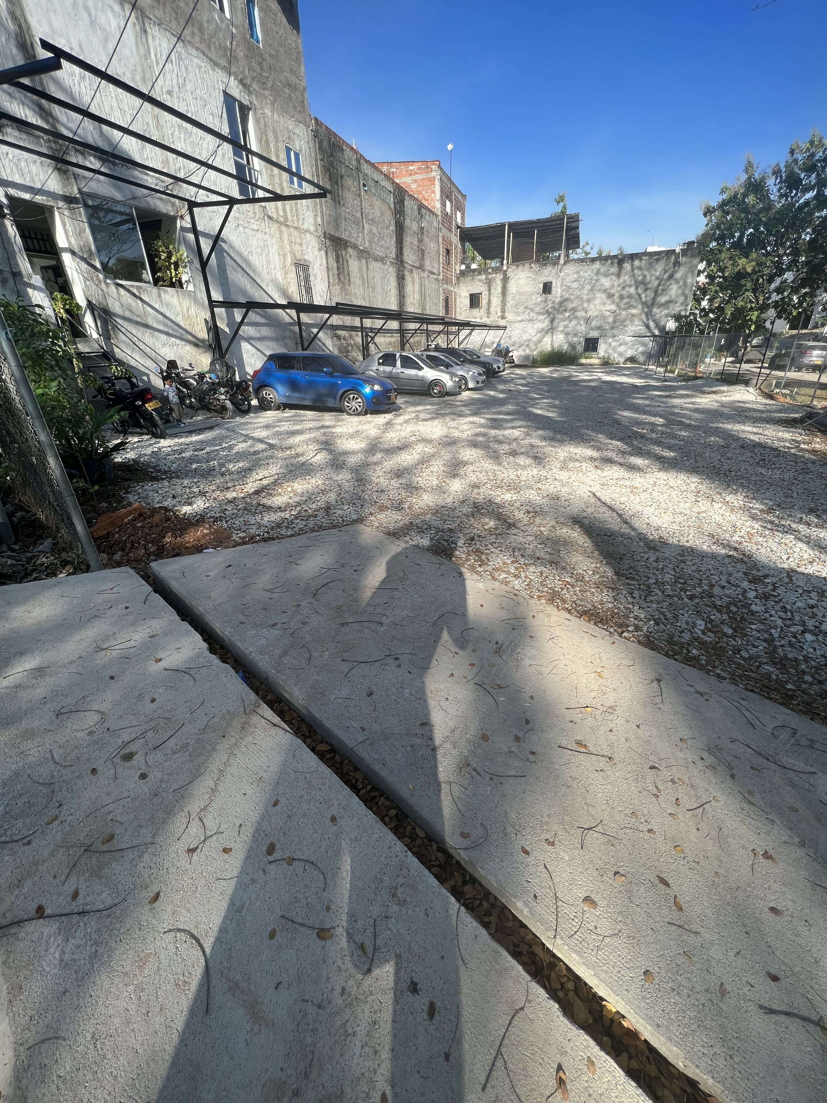 A parking area with several cars and motorcycles, a concrete building with a metal structure, and a clear blue sky.