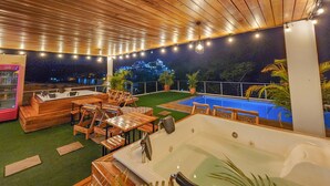 An outdoor pool area with wooden furniture and a hot tub, surrounded by a wooden ceiling and string lights. - MIRADORES DEL PARAISO  (Puerto Triunfo)
