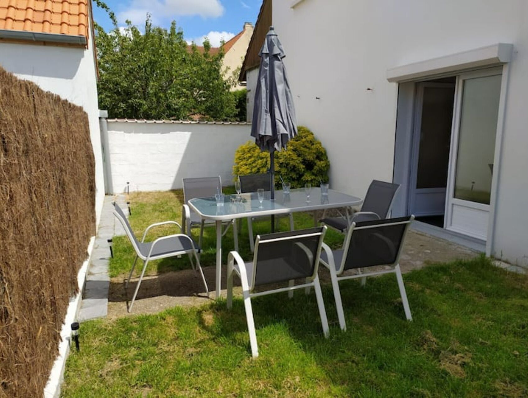 A patio with a table and chairs, a small umbrella, and a door leading to a covered area.