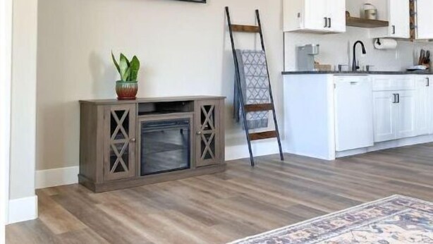 A modern living room with a flat-screen TV, a fireplace, a dining area with white cabinets, and a patterned rug.