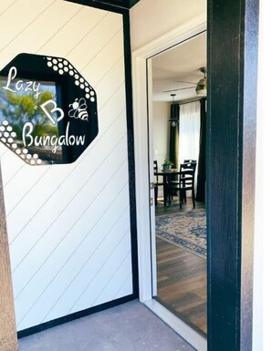 Käytävässä on kyltti, jossa lukee ”Lazy Bungalow”, ja käytävältä avautuu näkymä ruokailutilaan, jossa on pöytä ja tuoleja.