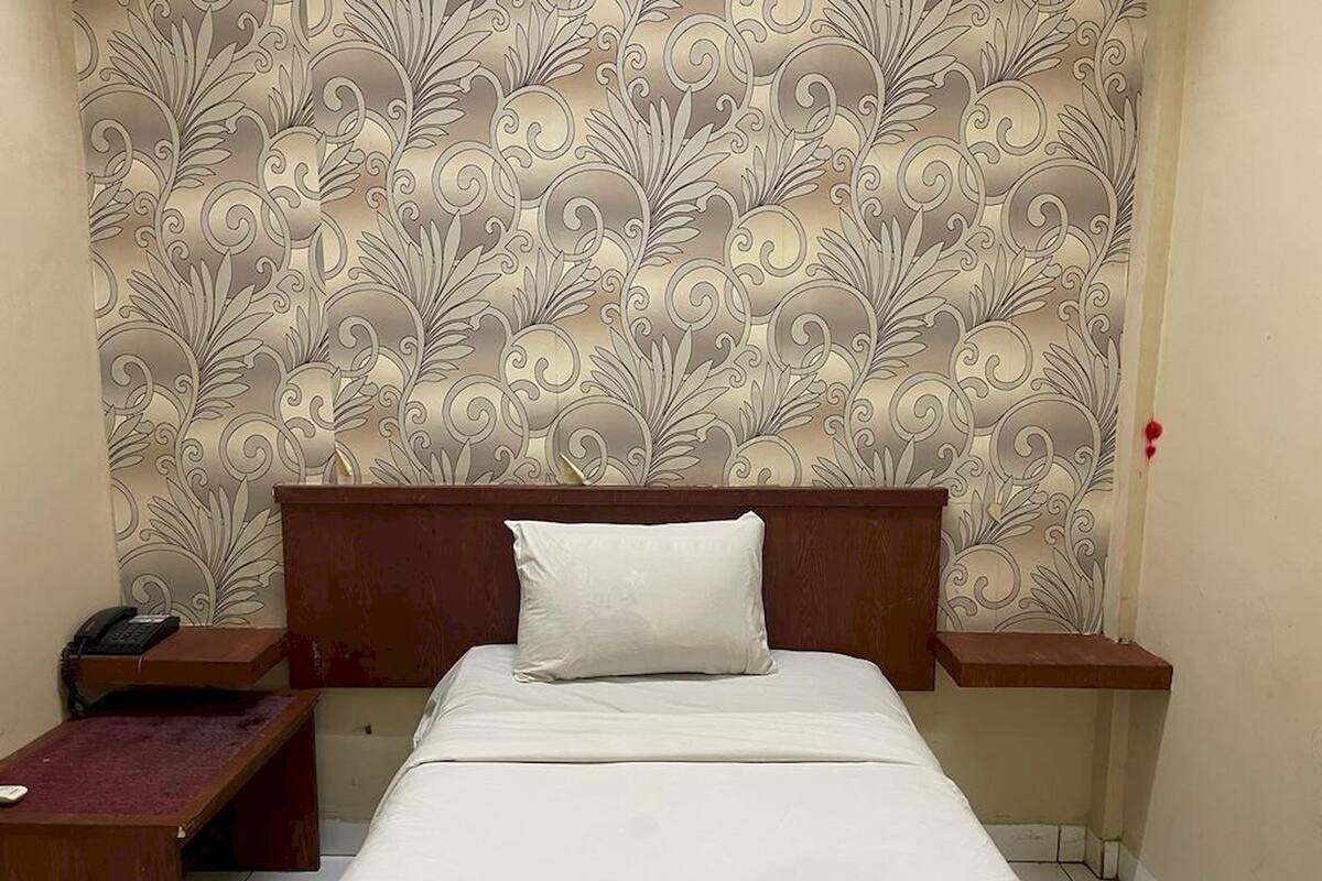 Een hotelkamer met een bed, nachtkastje, telefoon en een decoratief behangpatroon.