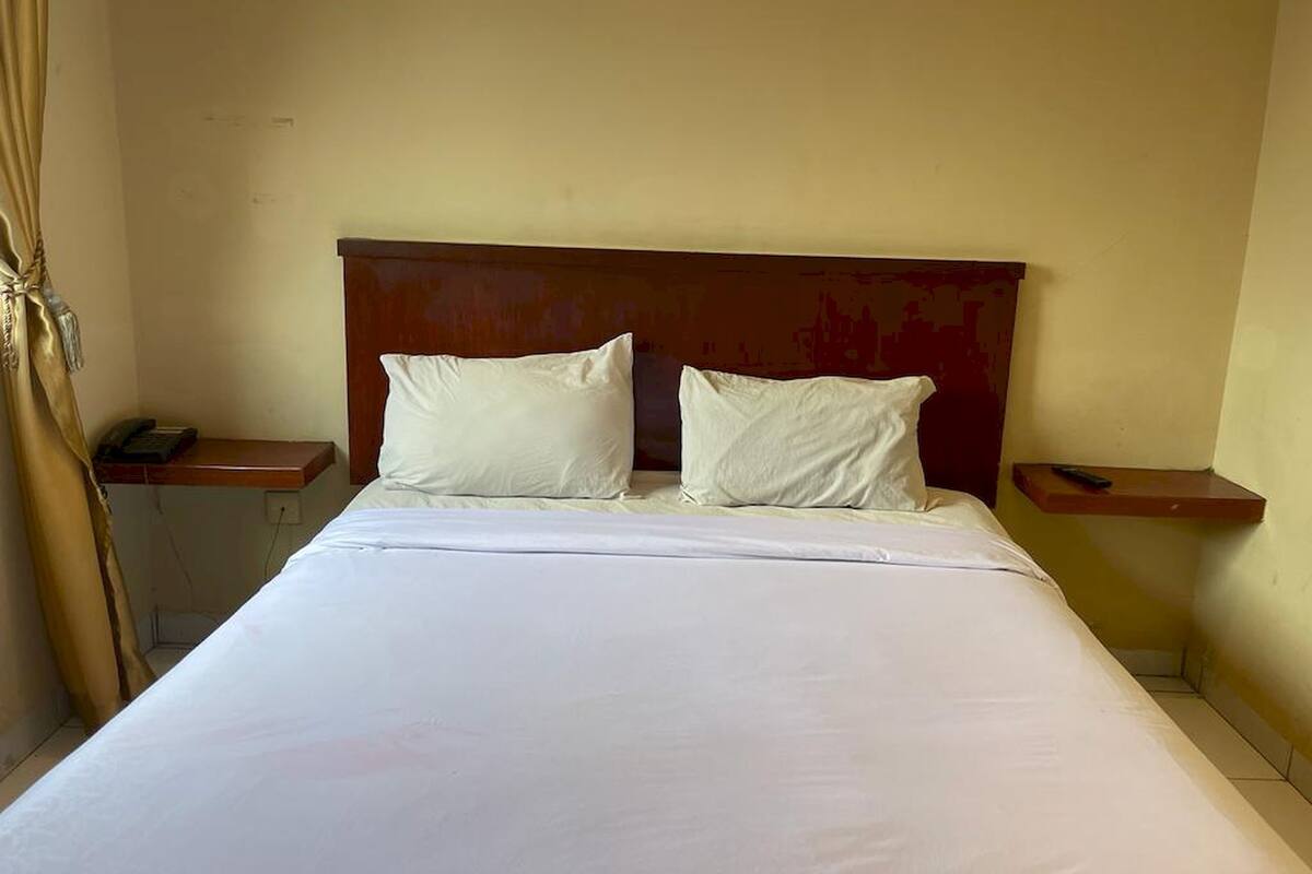Hotelkamer met een groot bed, twee kussens, een houten hoofdbord en nachtkastjes met lampen.