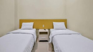 A twin room with two single beds, a wooden headboard, a small bedside table with a drawer, and a wall-mounted light fixture. - Capital O 93285 Residence Hotel Syariah (Medan)