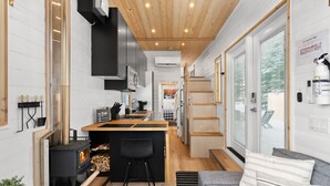 Une cuisine moderne dotée d’un îlot central, d’un poêle à bois encastré et d’un coin salon confortable avec un canapé et des coussins.