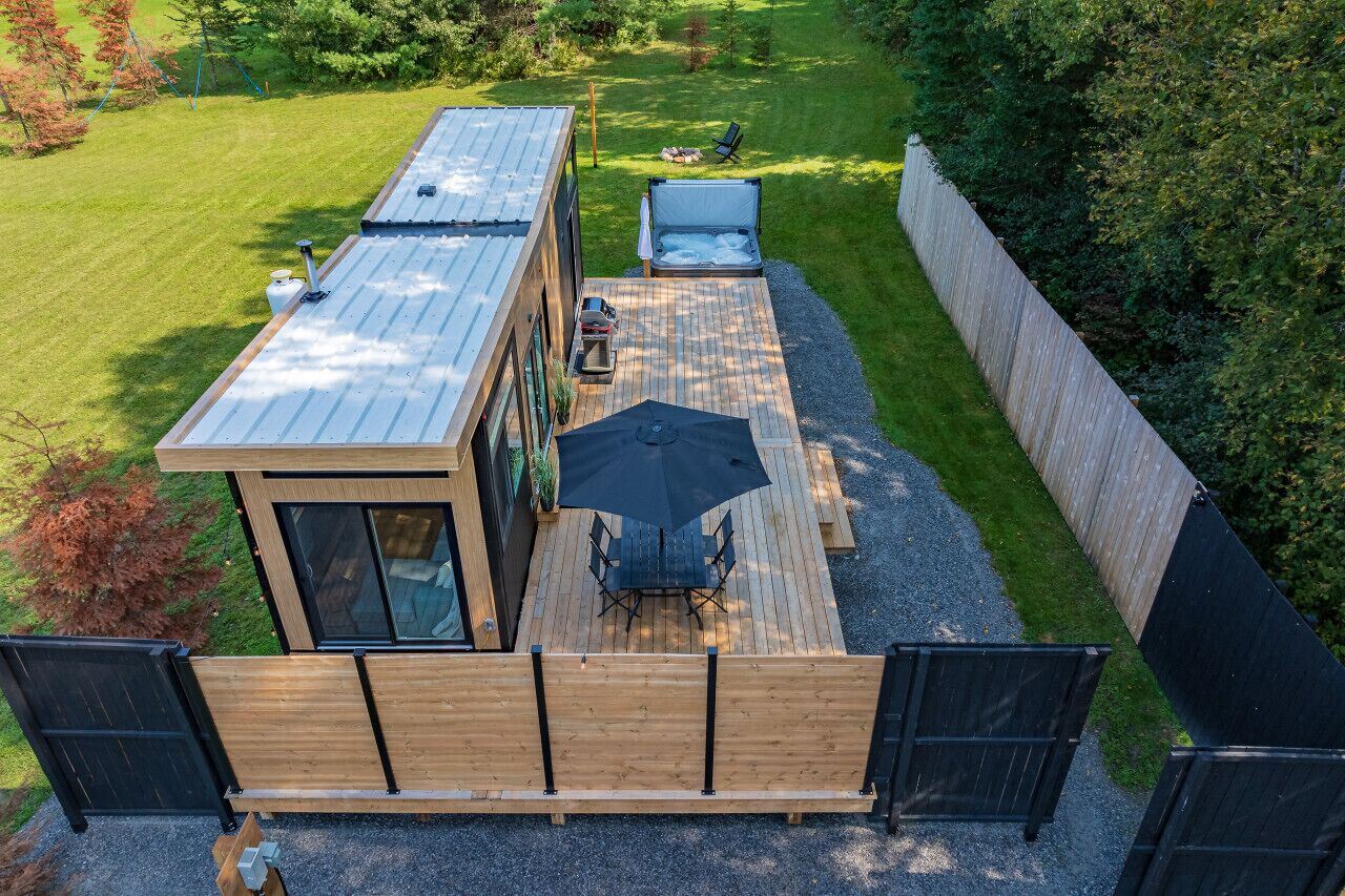 Eine moderne Außenterrasse mit Holztisch und -stühlen, einem Whirlpool und einer kleinen Holzkonstruktion.
