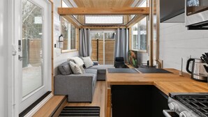 Une cuisine compacte dotée d’un plan de travail en bois, d’une cuisinière intégrée et d’un coin repas avec un canapé gris et une petite table.