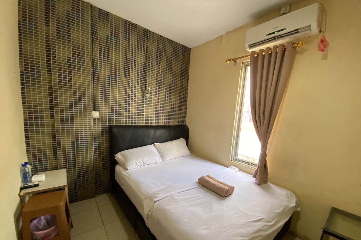 Een hotelkamer met een bed, een raam met gordijnen, een airconditioning en een betegelde muur.