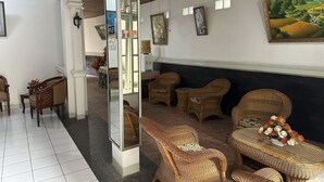 A lobby with wicker furniture, a large mirror, and a painting on the wall. - Capital O 93291 Bintang Hotel (Padang)