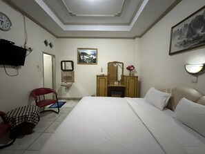 Ein Hotelzimmer mit einem Bett, einem Schreibtisch mit Spiegel, einem Sessel, einem Waschbecken und einem Fernseher.