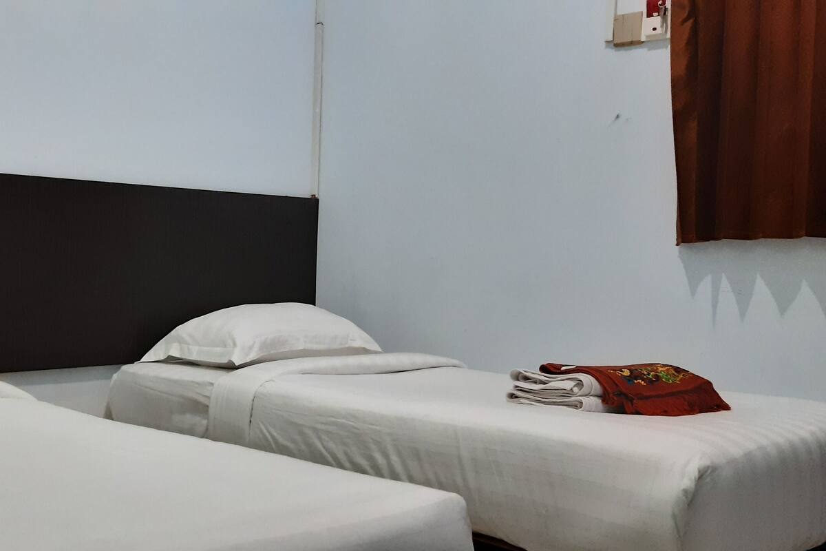 Een kamer met twee enkele bedden, wit beddengoed, een zwart hoofdeinde en een rode tas op een van de bedden.