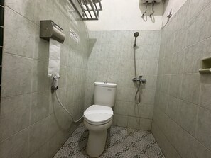 Ein kleines Badezimmer mit Fliesen, einer Toilette, einer Dusche und einem Papierhandtuchspender.