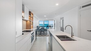 A modern kitchen with a central island, built-in shelves, and a view to the ocean.