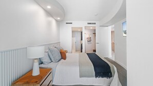 A modern hotel room with a neatly made bed, a bedside table with a lamp, and a view of the hallway.