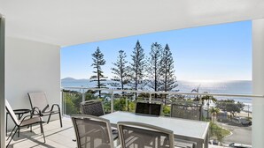 A balcony with a table and chairs, overlooking a scenic view of trees and a body of water.