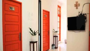 A hallway with red doors, a potted plant, a trash bin, and a television mounted on the wall.