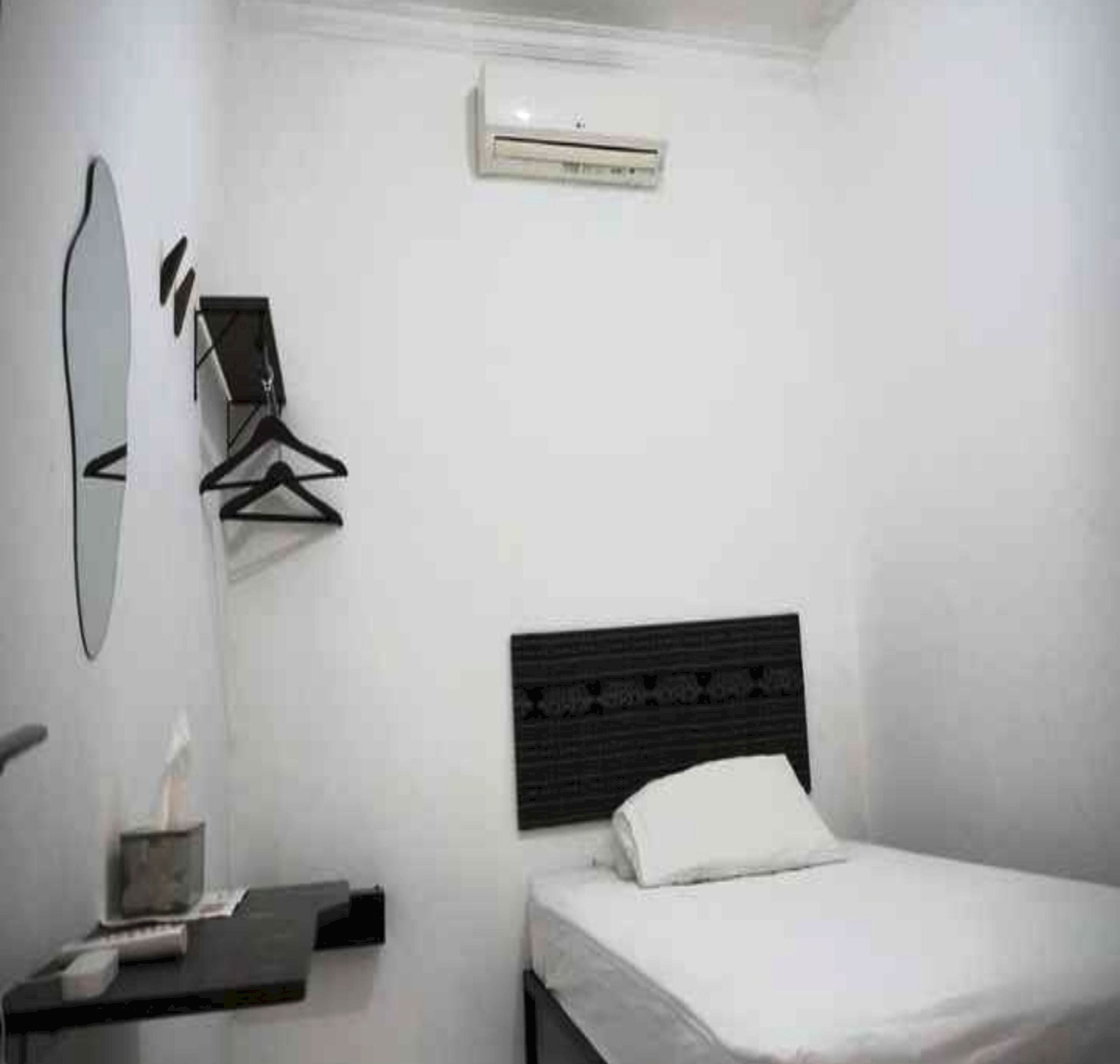 A small, clean room with a bed, a bedside table, a mirror, and a wall-mounted air conditioner.