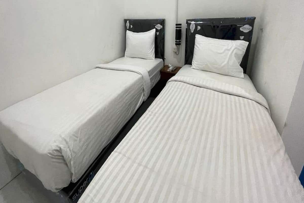 A small, compact room with two single beds, each with a headboard and a bedside table.