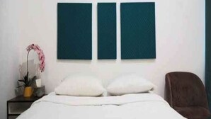 A bedroom with a bed, two pillows, a nightstand with a plant, and a chair.