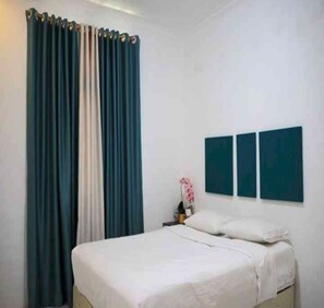 Une chambre à coucher avec un lit, une table de chevet, une lampe et une fenêtre avec des rideaux.