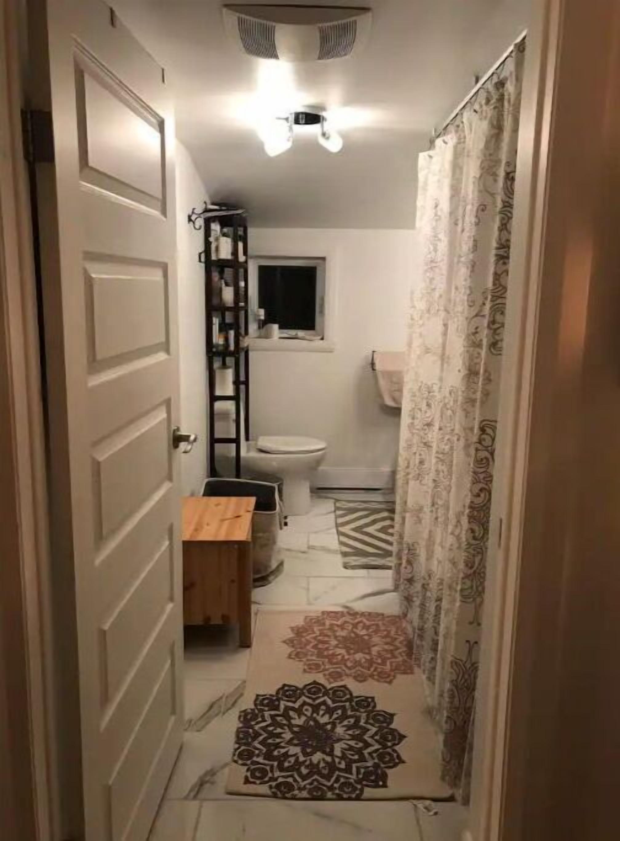 A narrow hallway leading to a bathroom with a toilet, a small window, and a shelf with toiletries.
