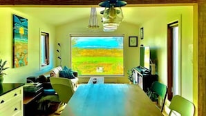 Un'area pranzo con un tavolo lungo, sedie, un lampadario e un'ampia finestra vista su un campo verde.