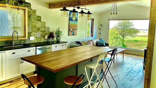 Una cucina moderna con isola in legno, mobili bianchi e un'ampia finestra con vista sull'esterno.