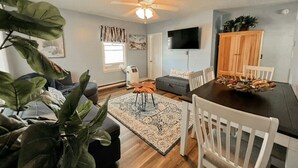 A living room with a dining table, chairs, a ceiling fan, a TV, a fireplace, and a large plant. - 5 Bedroom House Steps to the Beach (Old Orchard Beach)