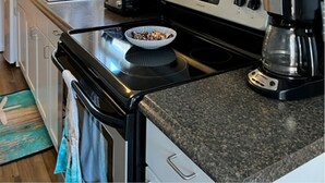 A kitchen with white cabinets, a black stove, a coffee maker, and a bowl on the counter. - 5 Bedroom House Steps to the Beach (Old Orchard Beach)