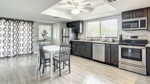 A modern kitchen with a dining area, featuring a ceiling fan, stainless steel appliances, and a large window.