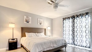 A bedroom with a bed, bedside lamps, a ceiling fan, and a window with patterned curtains.