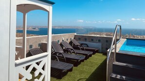 Un área de piscina en la azotea con sillones y vista al mar.