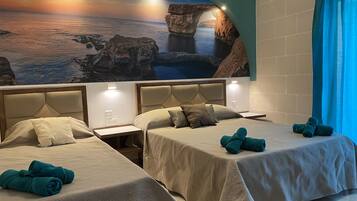Habitación de hotel con dos camas, un amplio mural de una escena costera y vistas al mar a través de una ventana.