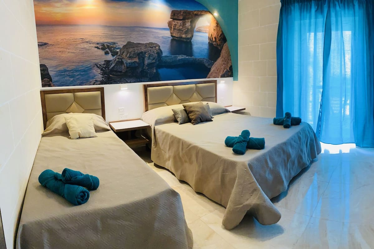Habitación de hotel con dos camas, un escritorio, un armario y un gran mural panorámico en la pared.